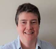 Census director Nicola Tyson-Payne smiling in a blue striped shirt, standing against a white wall