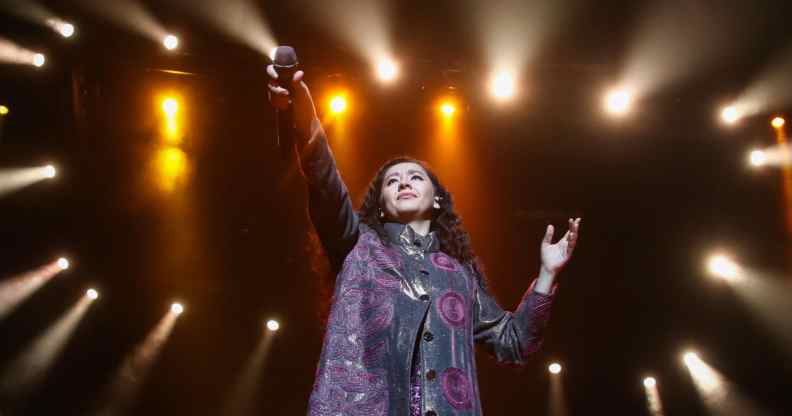 Manizha Sangin holds her microphone in the air against a constellation of spotlights