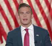 Madison Cawthorn addresses the virtual 2020 Republican National Convention, wearing a navy suit, white shirt and red tie against the stripes of the American flag