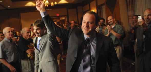 Jared Polis (R) and Marlon Reis hold hands as people clap behind them