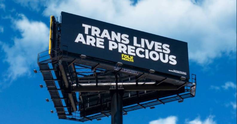 Three billboards in a triangle formation. The front one is visible and reads: Trans lives are precious