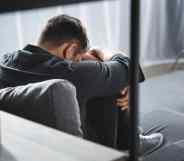 back view of man with panic attack crying and hugging legs in apartment