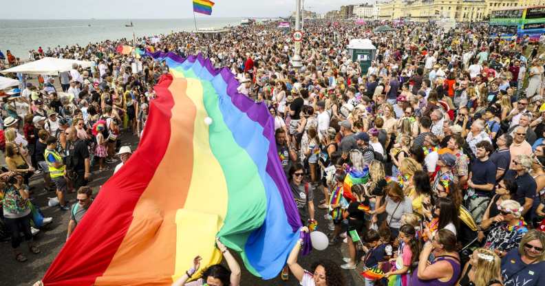 A crowd of pride goers with a giant, long rainbow banner stretching through the crowd