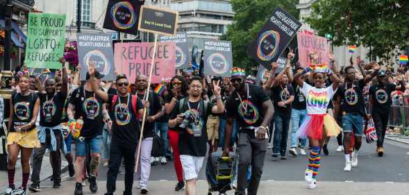 A crowd of mostly Black and brown LGBT+ protesters holding placards with messages like "refugee pride" and "be proud to support LGBTQ refugees"