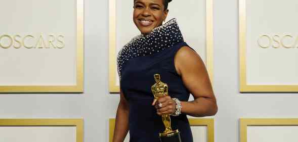 Mia Neal triumphantly holds her Oscar award in a navy dress on the Oscars red carpet