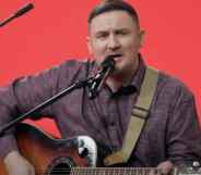 Dmitry Butakov sings while strumming the guitar against a red background