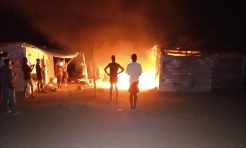 A photo of two shelters, one with flames spilling out of its door