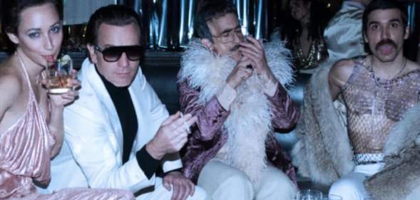 Ewan McGregor as Halston, sat with a woman, a man in a feather boa and another man in a mesh top