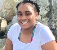 Mikayla Miller smiles in a white top, sat by some rocks