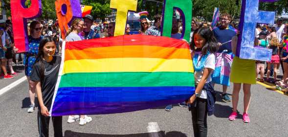 Two girls lead a segment of the parade with a rainbow flag followed by adults with the word 'PRIDE' during the Portland Pride Parade