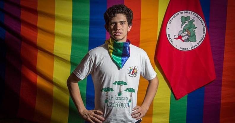 Lindolfo Kosmaski stands with his hands on his hips against the LGBT+ Pride and Landless Workers' Movement flags