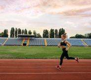 Female runner in sportswear jogging, training on stadium. Woman doing stretching exercise before running on outdoor arena