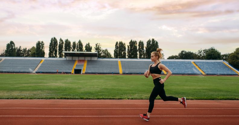 Female runner in sportswear jogging, training on stadium. Woman doing stretching exercise before running on outdoor arena