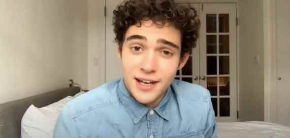 Joshua Bassett speaks to the camera in a denim shirt in a white living room