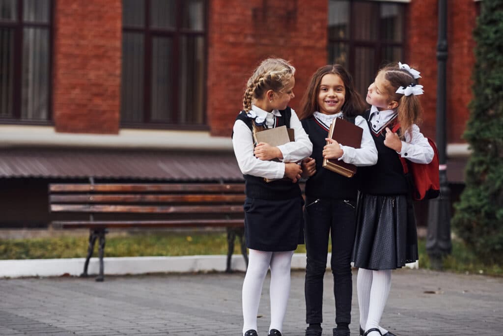 Group of female kids in school uniform that is outdoors together near education building