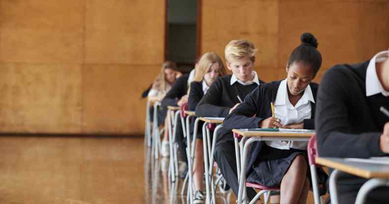 Teenage Students In Uniform Sitting Examination In School Hall