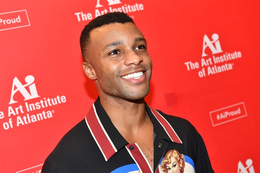 Dyllón Burnside smiling, wearing a black shirt with a red collar, in front of a red backdrop