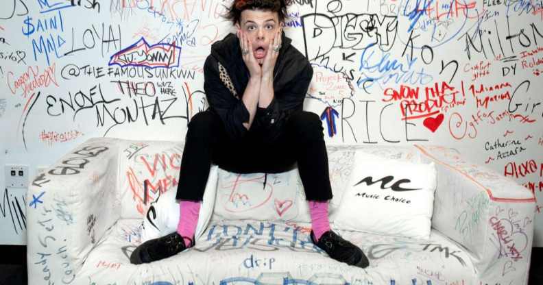 Yungblud, real name Dominic Harrison, visits Music Choice in 2019 and poses against a background of graffiti while sitting on a sofa