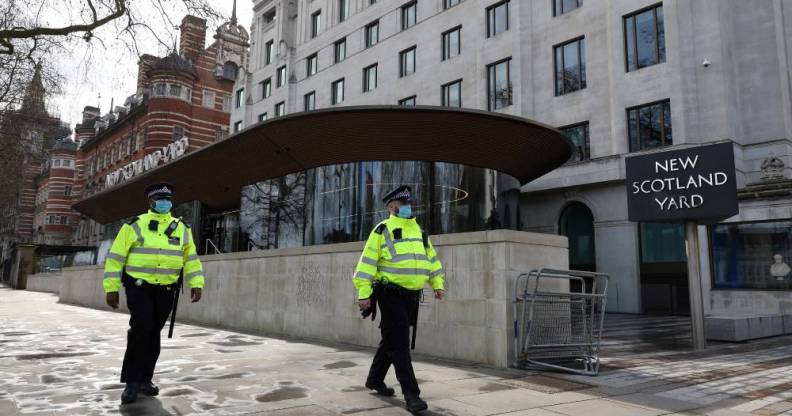 Police officers wearing face coverings due to Covid-19 walk past New Scotland Yard, the headquarters of the Metropolitan Police Service