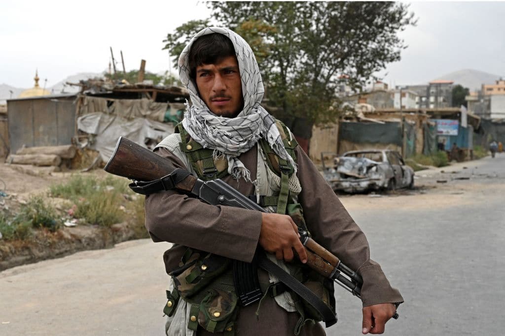 A Taliban fighter stands guard near a damaged car after multiple rockets were fired in Kabul on August 30, 2021.