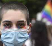 A protester with the face painted in the LGTBQ flag colours