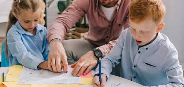 Teacher in eyeglasses helping preschoolers with drawing at table in classroom