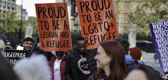 Protesters buttress placards up high standing in solidarity with queer refugees in Parliament Square