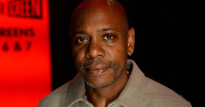 Dave Chappelle wears a neutral coloured shirt amid a black and red background