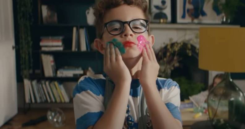 still from the latest John Lewis home insurance ad. The still depicts a young boy wearing a dress and colourful makeup smearing paint on his face