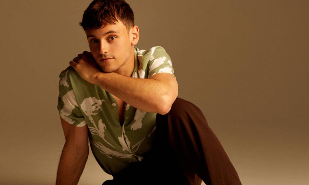 Tom Daley sits in front of a neutral colloured background