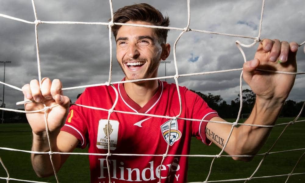 Adelaide United star Josh Cavallo poses in a football goal while wearing a red jersey