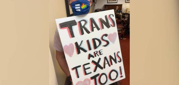 Hillary Moore-Embry holds up a sign that reads "Trans Kids are Texans Too!" in support of the trans community in Texas