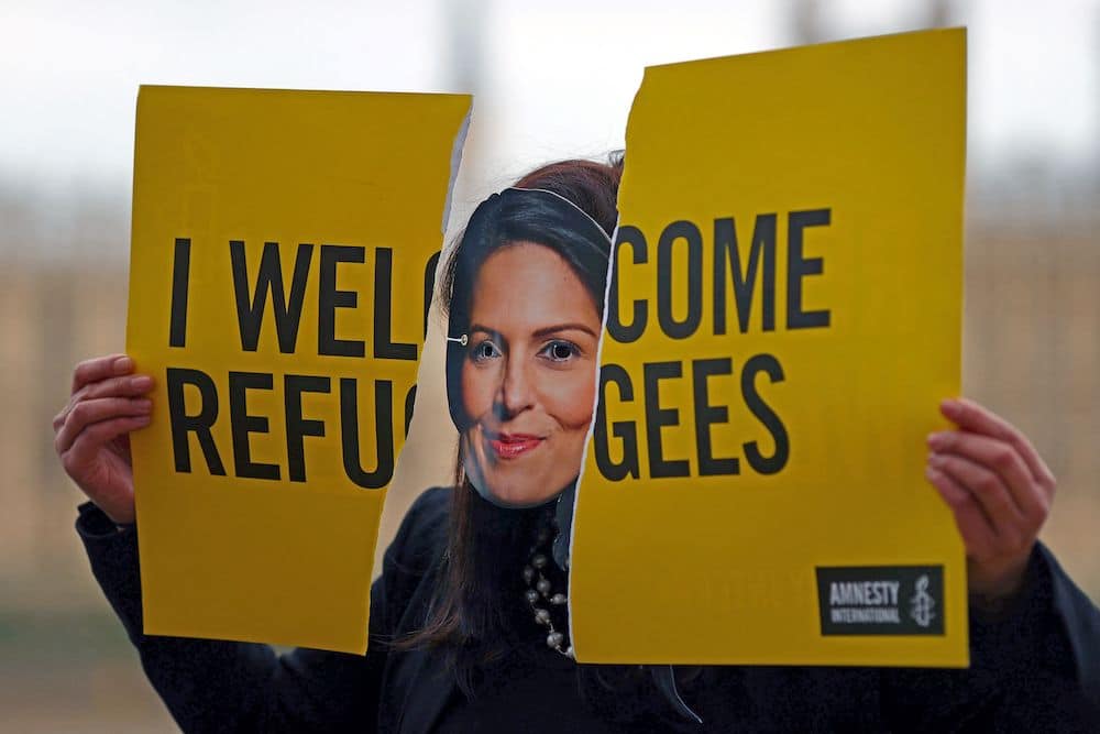 An activist from Amnesty International wears a mask depicting Britain's Home Secretary Priti Patel