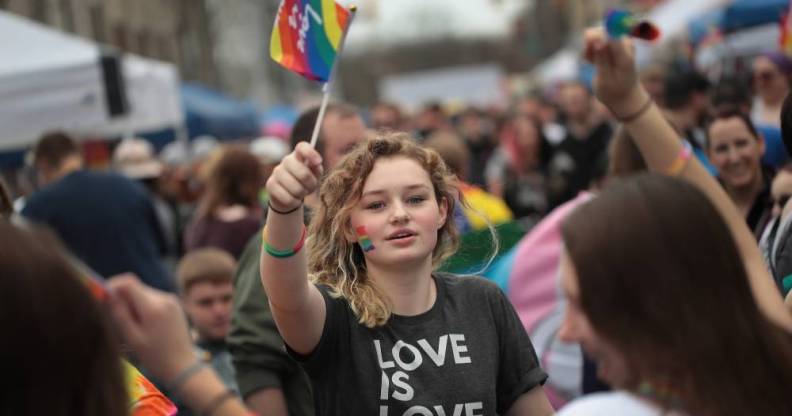 Young person holds up an LGBT+ pride flag while wearing a shirt that says 'love is love'