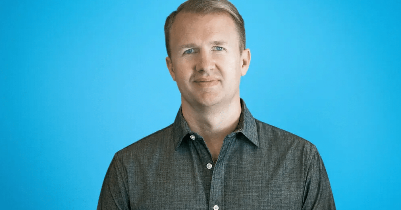 Jeff, wearing a dark grey shirt, smiling in front of a blue backdrop