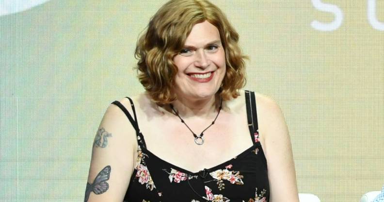 Lilly Wachowski wears a black patterned dress and sits in front of a grey-green background