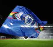 A flag bearer waves a Chelsea FC flag with the LGBT+ Progress flag design