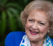 Betty White smiles at the camera while wearing a blue jacket and blue and white scarf