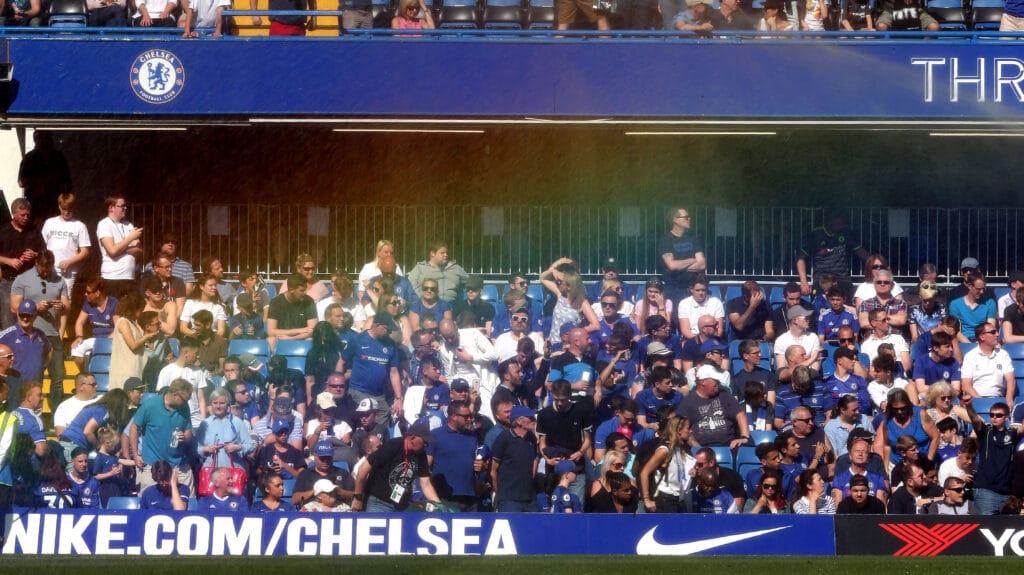 Water from the pitch sprinklers catches the light to form a rainbow in front of Chelsea fans during the Premier League match between Chelsea and Liverpool