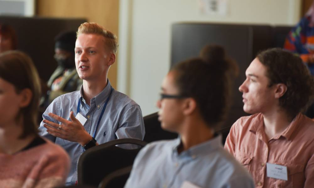 several people sit in conference chairs and listen to a person from the crowd talking