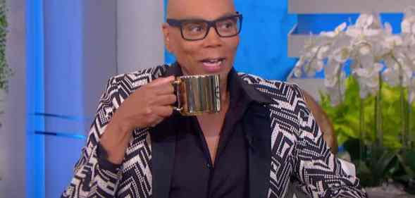 RuPaul appears on the Ellen DeGeneres show in a black, white and grey patterned suit, holding a gold coloured mug