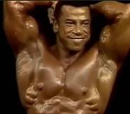 Chris Dickerson smiles and poses while flexing his muscles in a bodybuilding competition