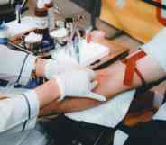 A medical professional uses a needle to try to draw blood from a person sitting in a chair wearing a light blue shirt