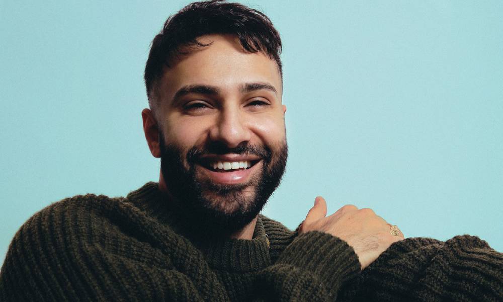 Zaher Saleh smiles at the camera while wearing an olive green jumper