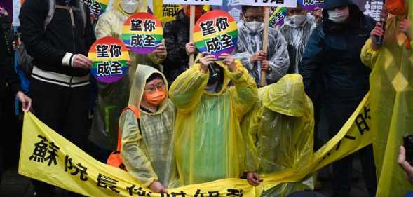 Joyce Chan (R) and Queenie Oyong (C) kneel down during the protest, holding circles with the rainbow flag