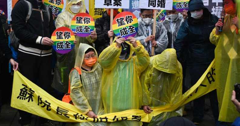 Joyce Chan (R) and Queenie Oyong (C) kneel down during the protest, holding circles with the rainbow flag