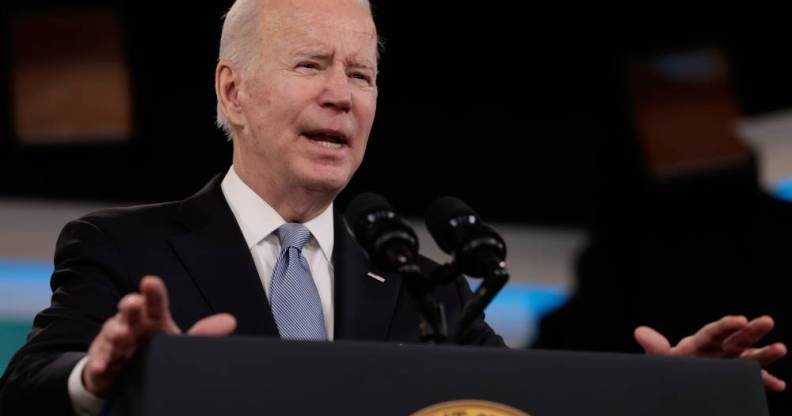 President Joe Biden, a white man, stands at a podium while wearing a dark suit jacket, white shirt and light blue tie