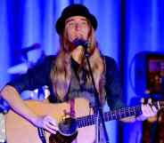 Sawyer Fredericks wears a bowler hat, grey vest and black long sleeved shirt as he sings and plays the guitar on stage