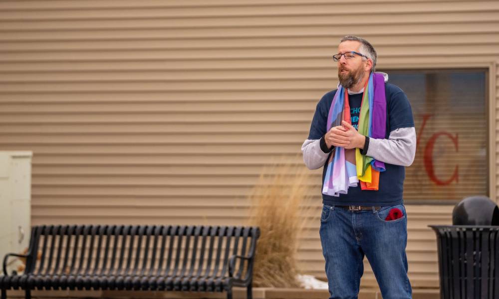 Mike Phelan wears a progressive Pride flag around his neck as his stands outside