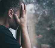 Man standing near a window and covers his face